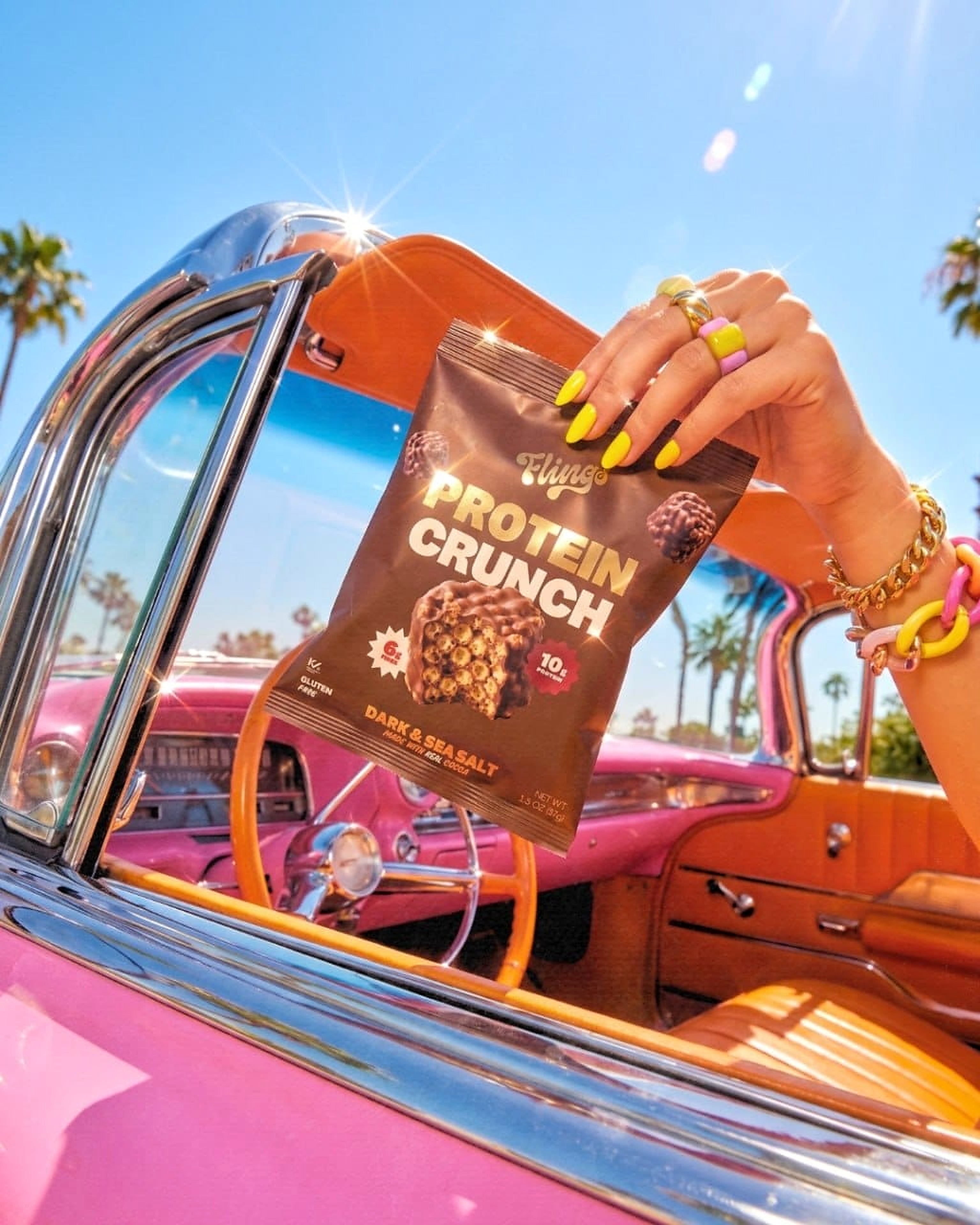 A hand holding a bag of Protein Crunch from a pink convertible